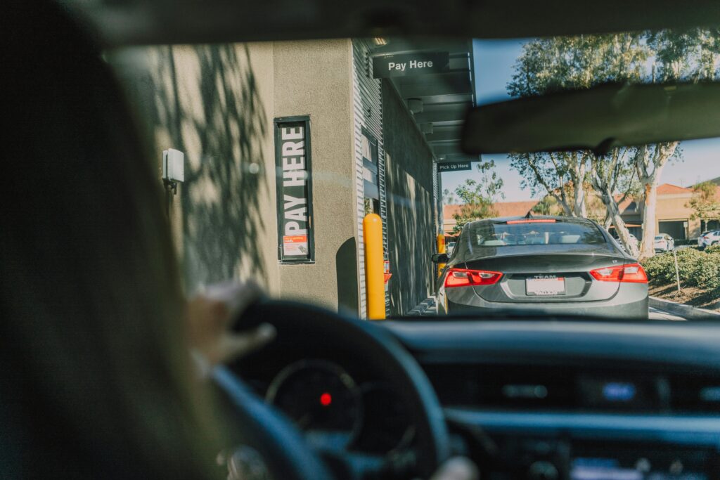 A driver's perspective waiting at a fast food drive-thru queue in daylight.